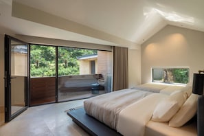 A bedroom with a large bed, a sliding glass door leading to a balcony, and a view of greenery outside.