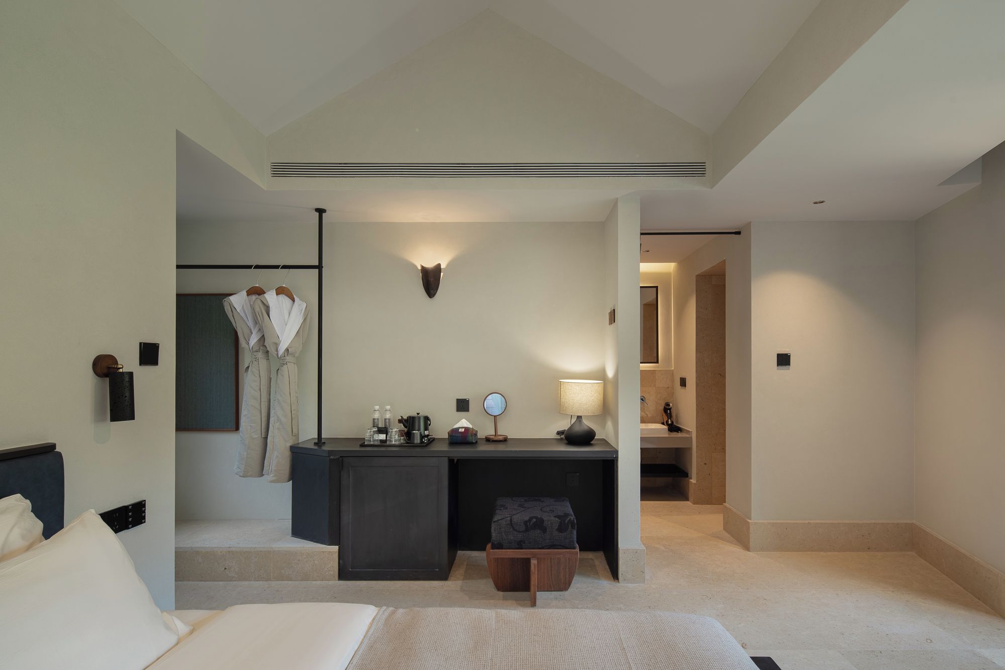 Habitación de hotel con cama, escritorio con lámpara, perchero y espejo.
