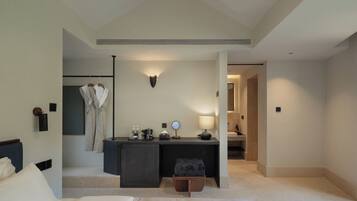 Habitación de hotel con cama, escritorio con lámpara, perchero y espejo.