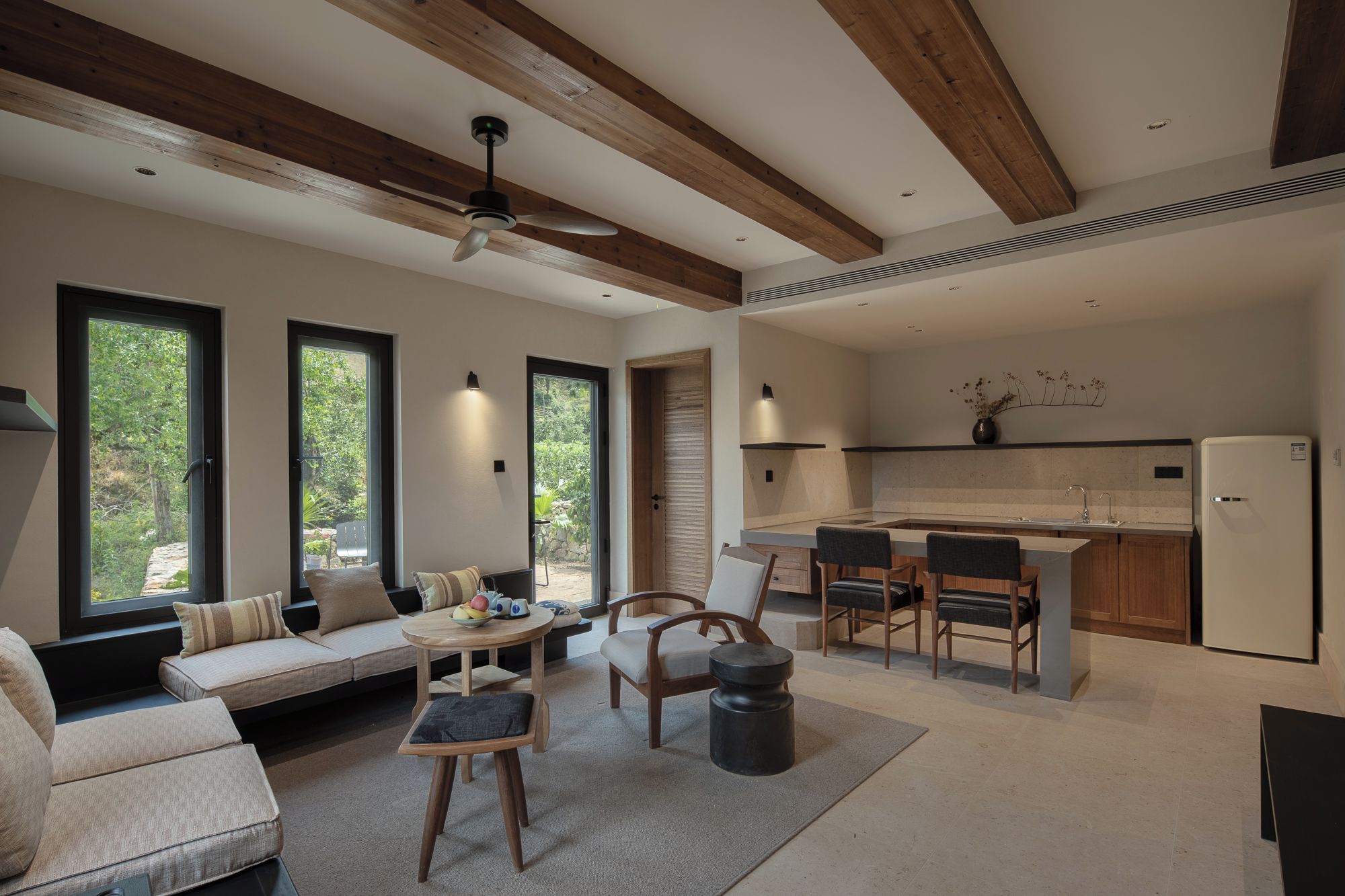A modern living room with a sofa, chairs, a dining table, and a kitchen area with a refrigerator and sink.