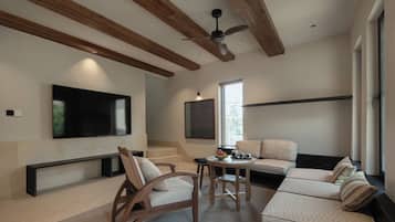 Una sala de estar moderna con televisor de pantalla plana, vigas de madera en el techo, ventilador de techo y una zona de estar con sofá y sillones.