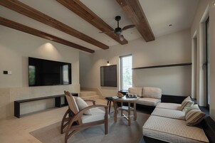 A modern living room with a flat-screen TV, wooden ceiling beams, a ceiling fan, and a seating area with a sofa and chairs.