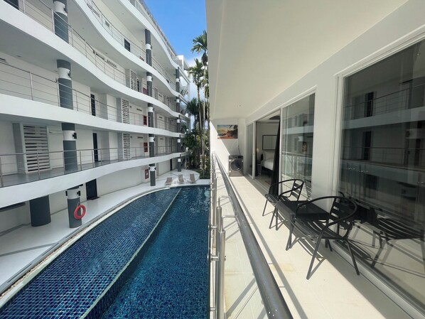 Un hotel moderno con zona de piscina, varios balcones y vistas a palmeras.