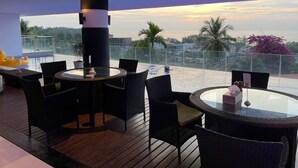 A rooftop terrace with round tables and chairs, a large cylindrical light fixture, and a view of the sunset over a cityscape. - B8 - 2 Bedrooms Serviced Apartment with pool view, Karon Beach (Tambon Karon)