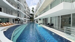A modern hotel with a central swimming pool, multiple balconies, and outdoor seating areas. - B8 - 2 Bedrooms Serviced Apartment with pool view, Karon Beach (Tambon Karon)