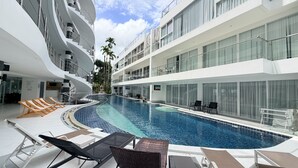 A modern hotel with a swimming pool, lounge chairs, and a multi-level balcony. - B8 - 2 Bedrooms Serviced Apartment with pool view, Karon Beach (Tambon Karon)