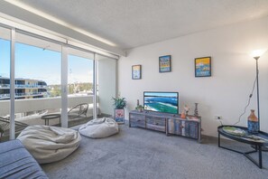 A modern living room with a large TV, comfortable seating, and a balcony with a view of the city. - Manly beach: Everything minutes away! (Manly)