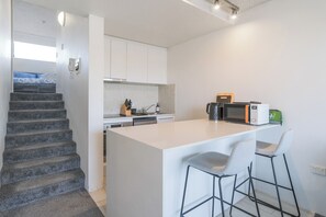 A modern kitchen with a central island, bar stools, a microwave, and a coffee maker. - Manly beach: Everything minutes away! (Manly)