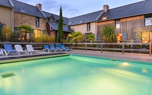 A swimming pool with lounge chairs, a wooden fence, and a stone building with a sloped roof. - Breton Alcove Stay for Six (Cancale)