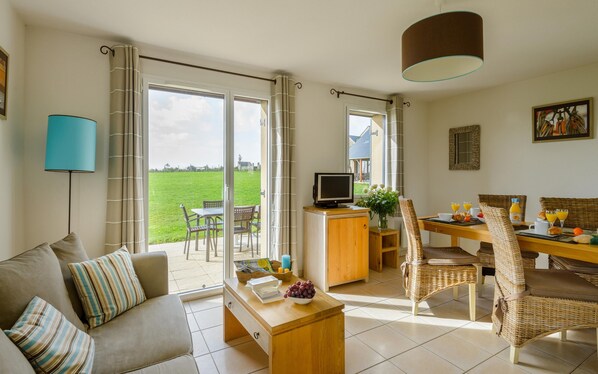 A living room with a sofa, a coffee table, a television, and a dining area with a table set for breakfast. - Breton Alcove Stay for Six (Cancale)