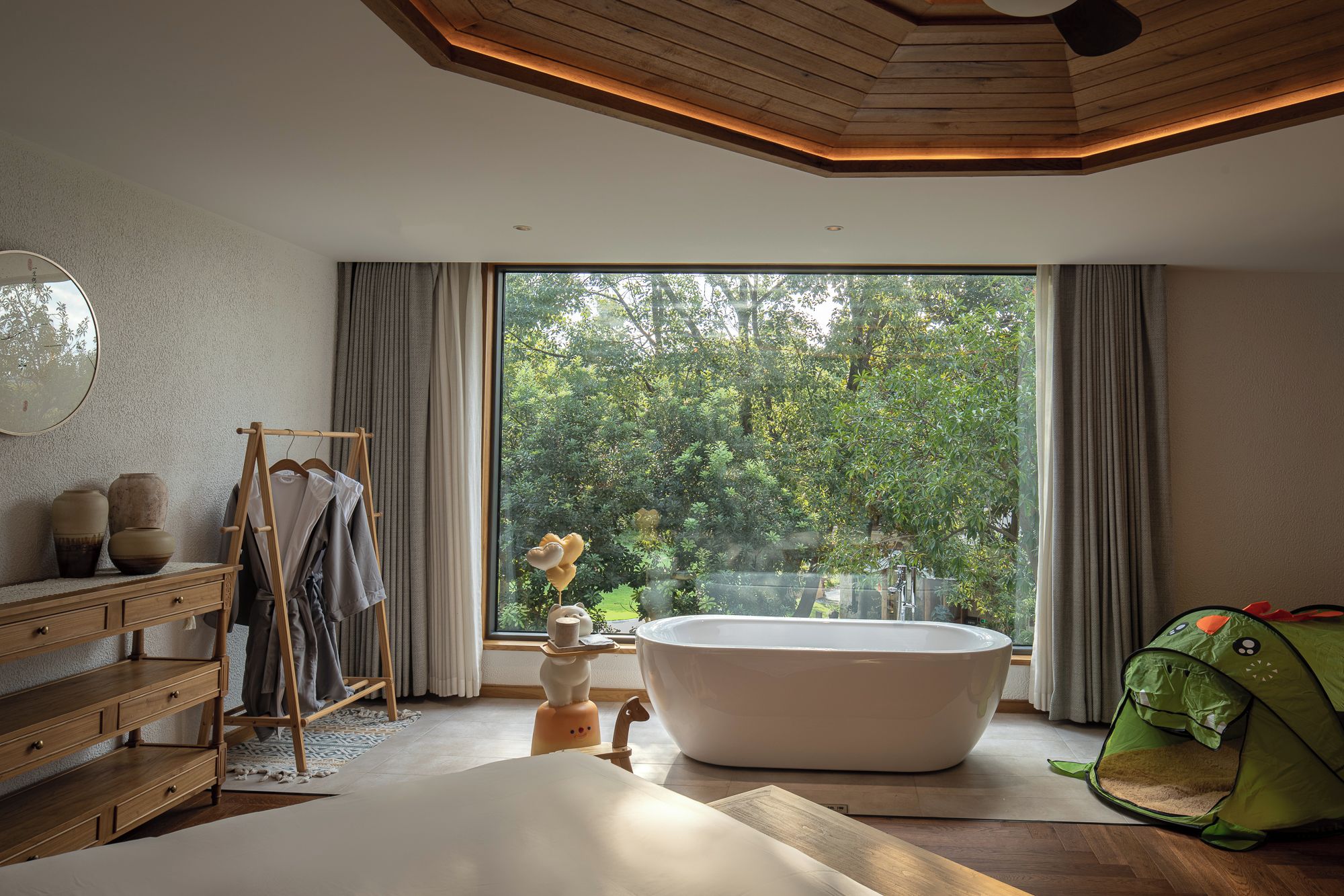 Ein modernes Badezimmer mit einer freistehenden Badewanne, einem Holzkosmetikschrank und einem großen Fenster mit Blick ins Grüne.