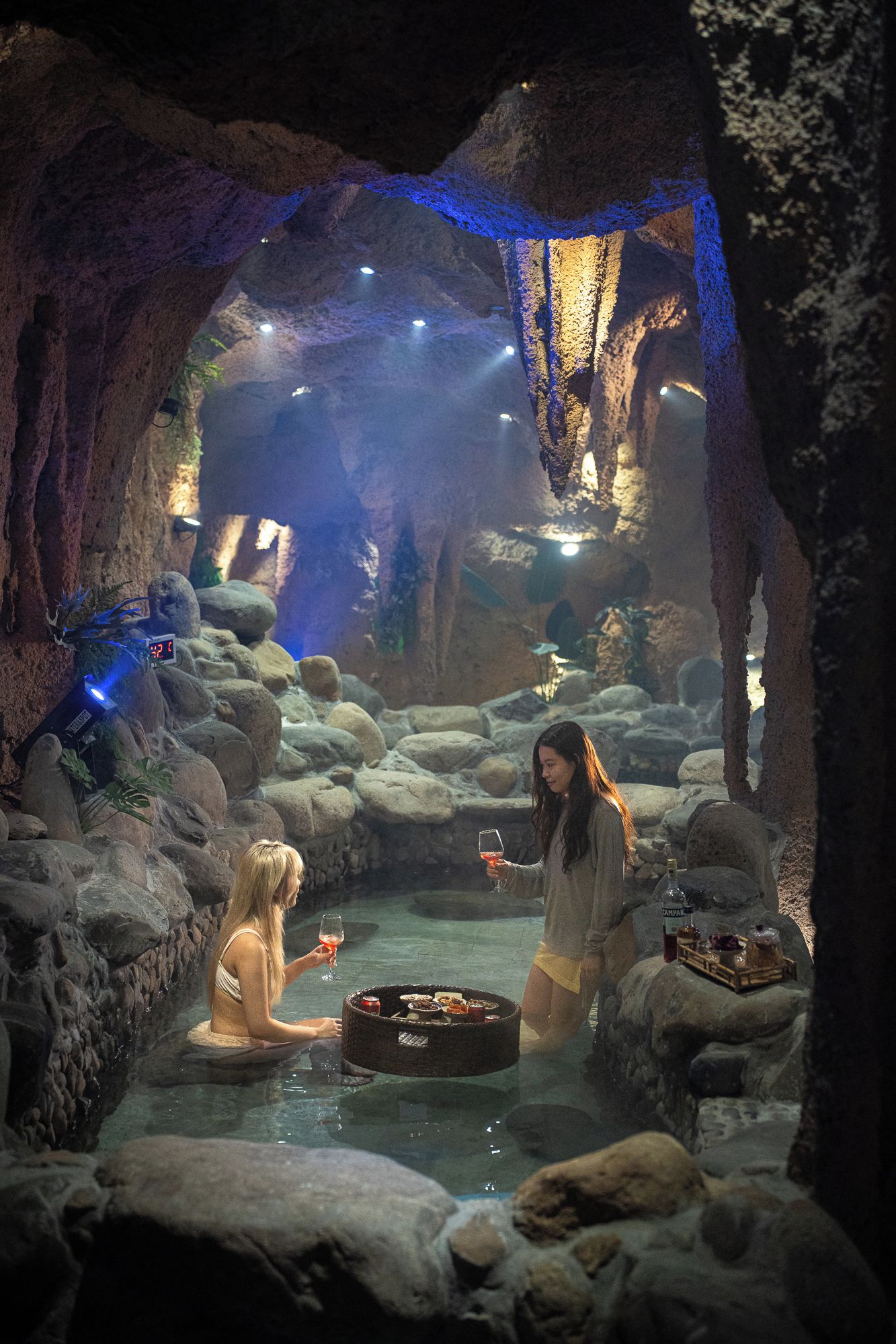 An indoor cave-like setting with a water feature, rocks, and a table with food and drinks.