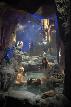 Ein Innenbereich, der einer Höhle ähnelt, mit einem Wasserspiel, Felsen und einem Tisch mit Speisen und Getränken.