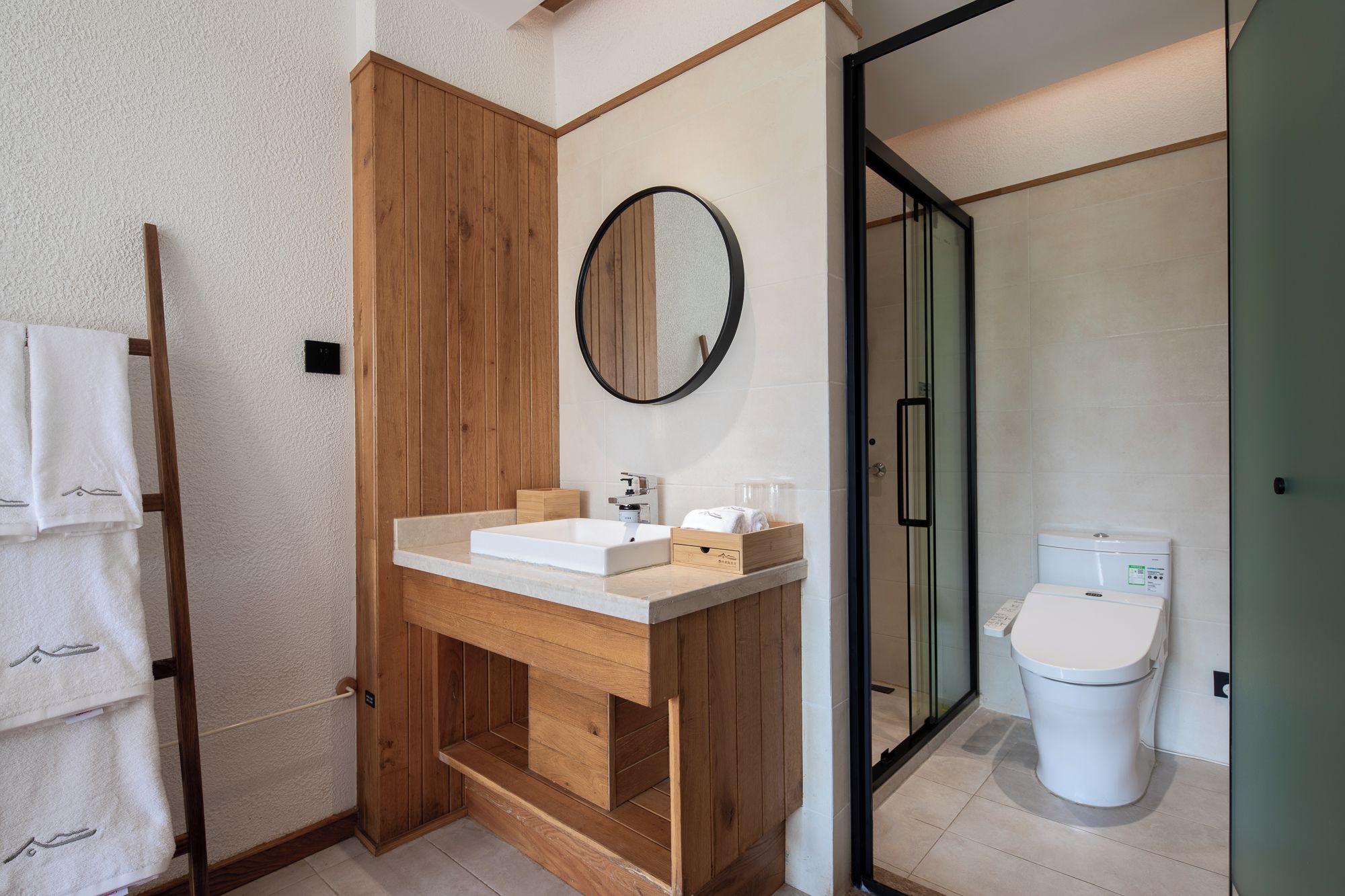 A modern bathroom with a wooden vanity, a round mirror, a white sink, and a toilet.