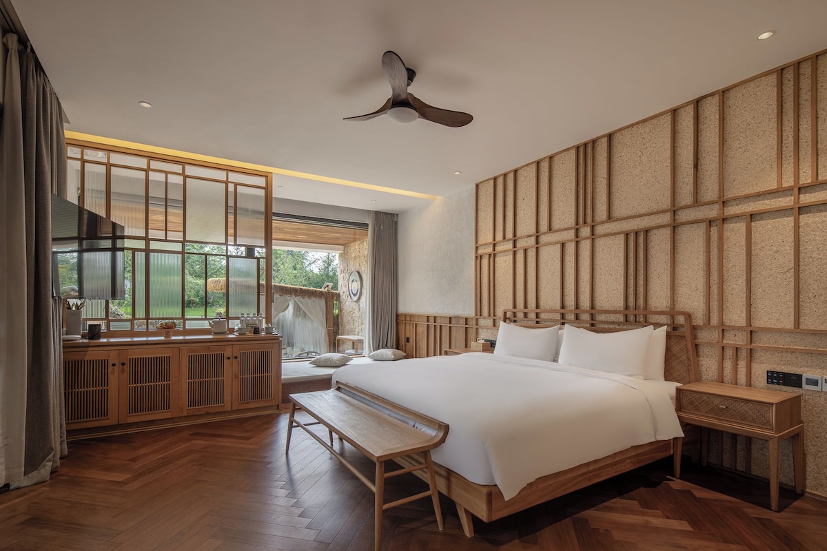 A modern bedroom with a large bed, wooden furniture, and a view of the outdoors.