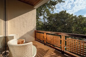 Ein Balkon mit einem Korbstuhl, einem Holztisch und Blick auf Bäume und Himmel.