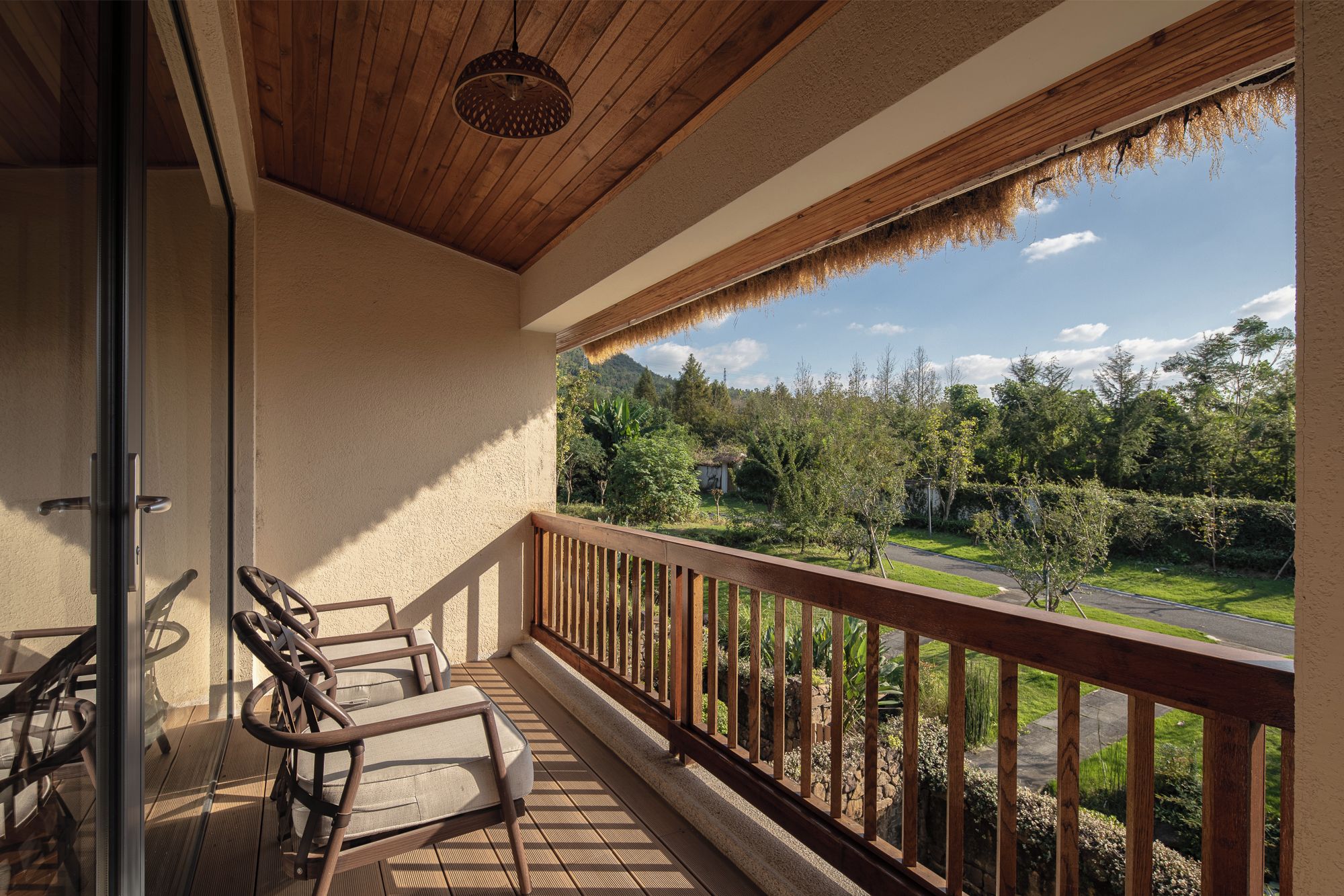 A balcony with a wooden railing, a glass door, and two wicker chairs.