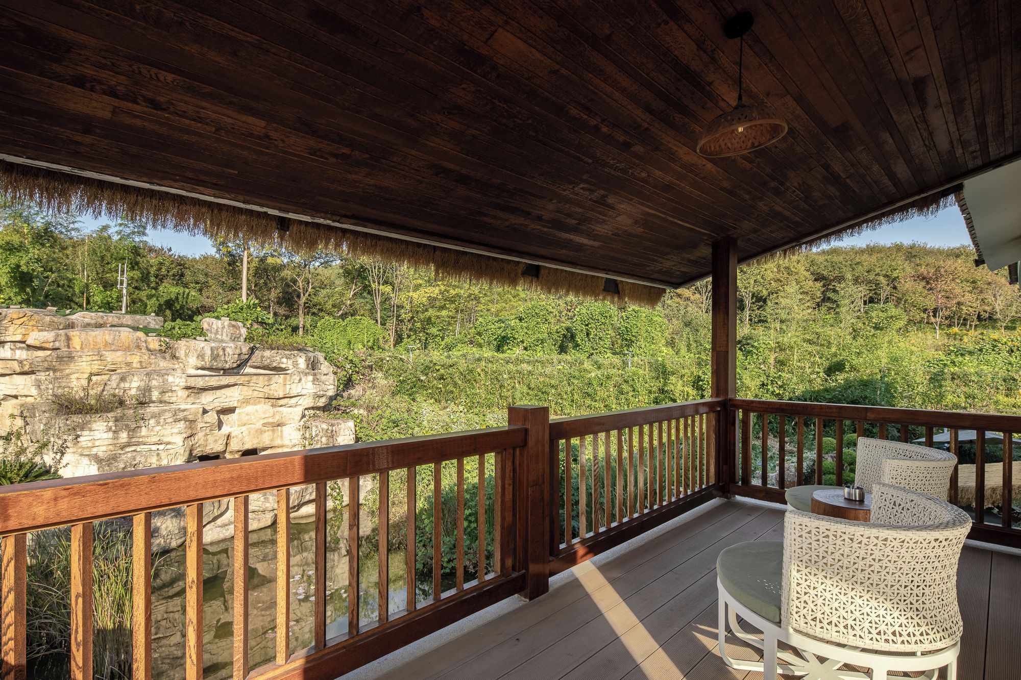 A wooden deck with a railing, overlooking a rocky landscape and dense greenery.