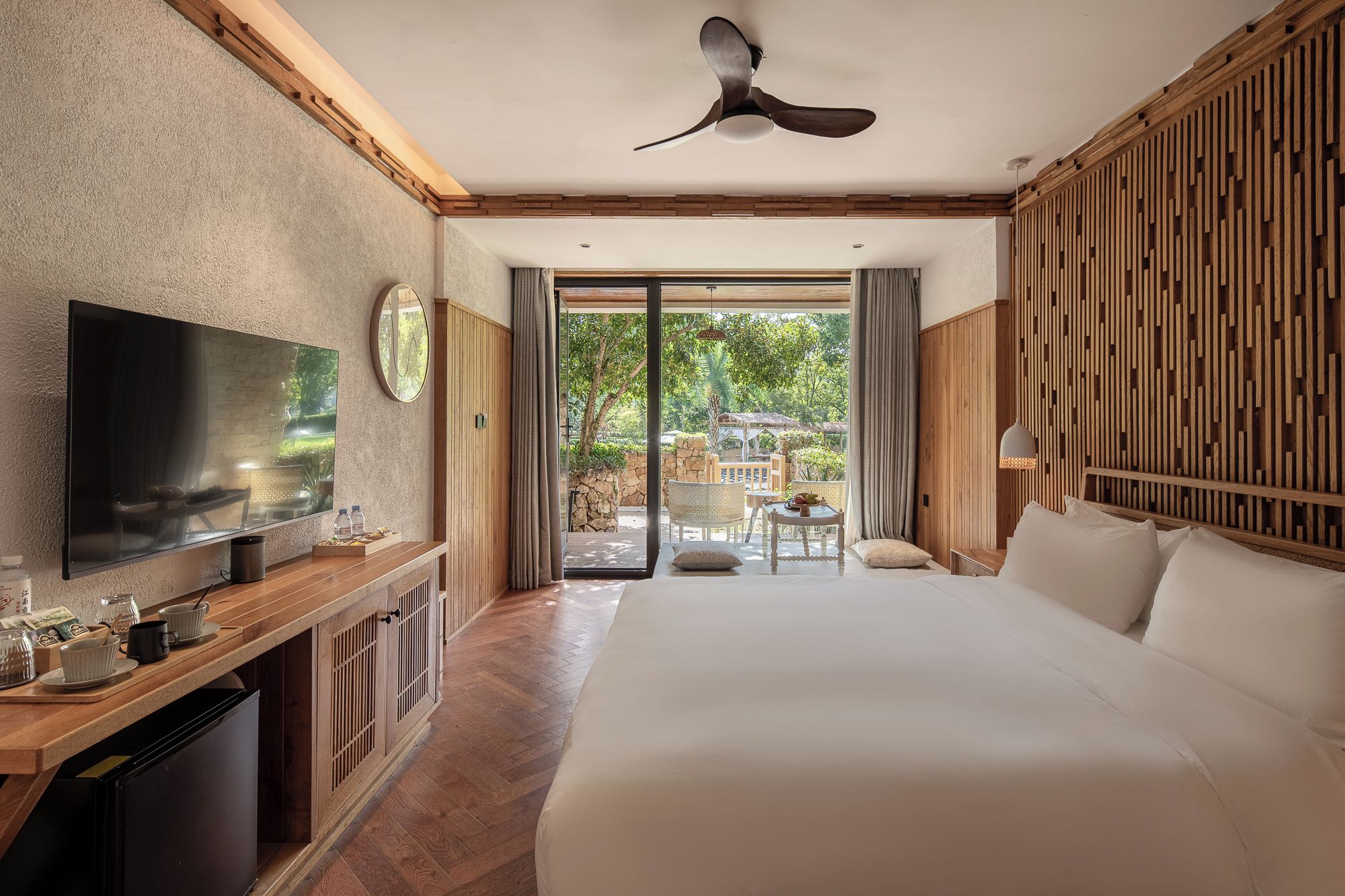 Ein Hotelzimmer mit einem großen Bett, einem Fernseher, einem Holztisch und Blick ins Freie.