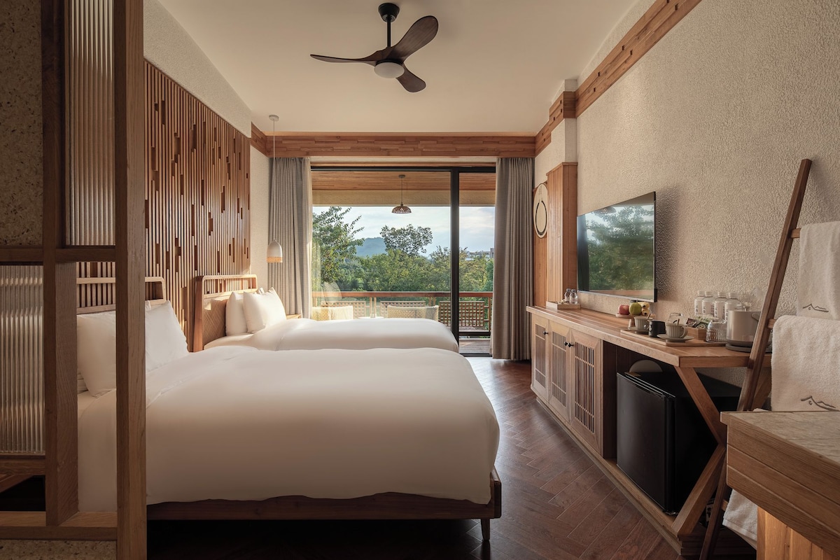 A hotel room with a bed, a desk, a television, and a balcony with a view.