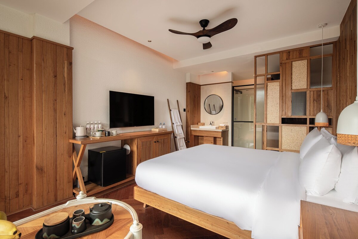 A hotel room with a bed, a television, a desk with a computer, a mirror, and a wooden wardrobe.
