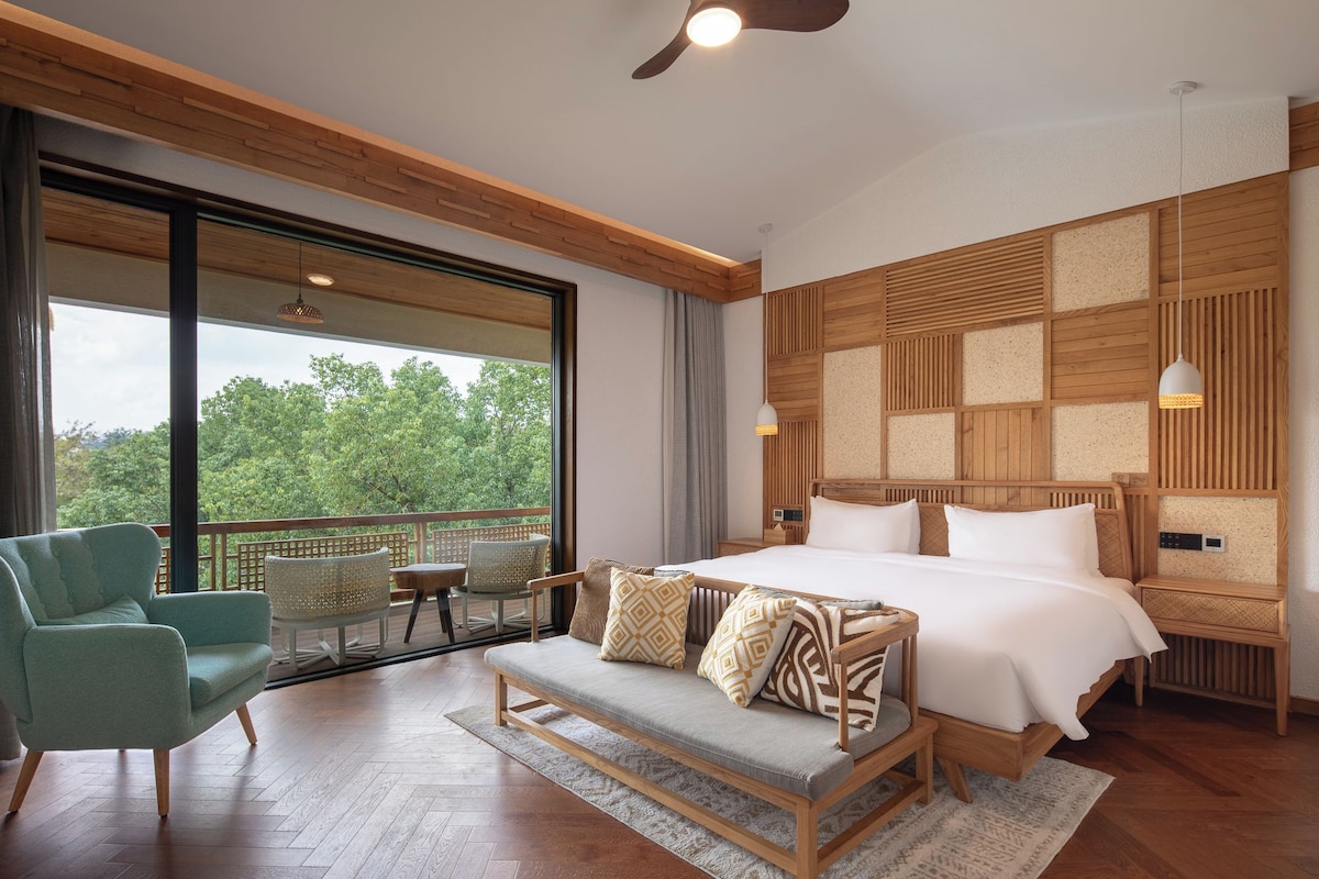 A modern bedroom with a large bed, a sofa, and a balcony with outdoor seating.