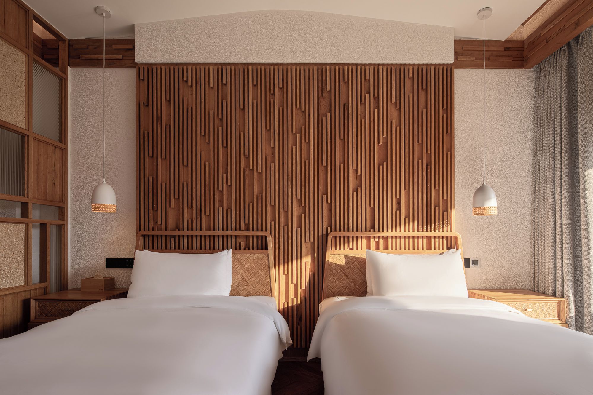 A hotel room with two beds, wooden panel wall, and pendant lights.