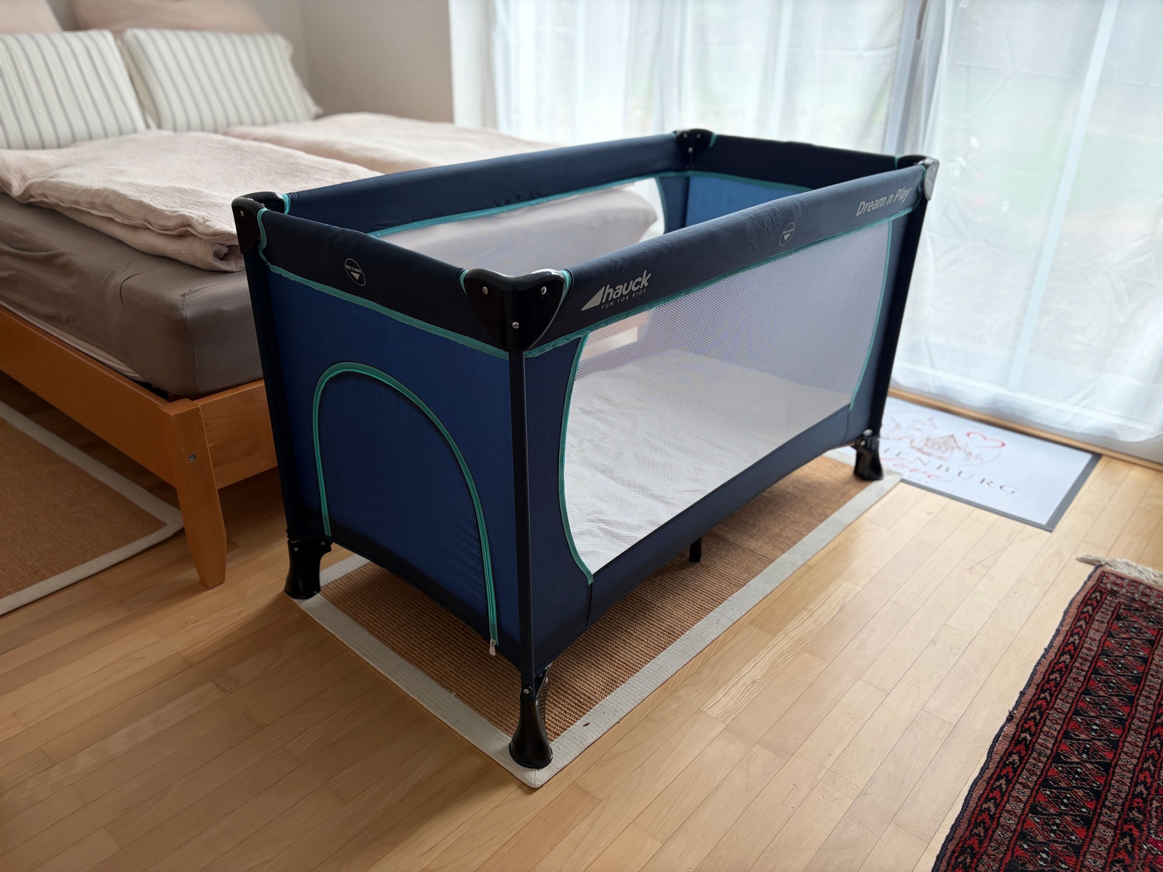 Een kamer met een bed, een zwart en blauw kinderbedje en een houten vloer.