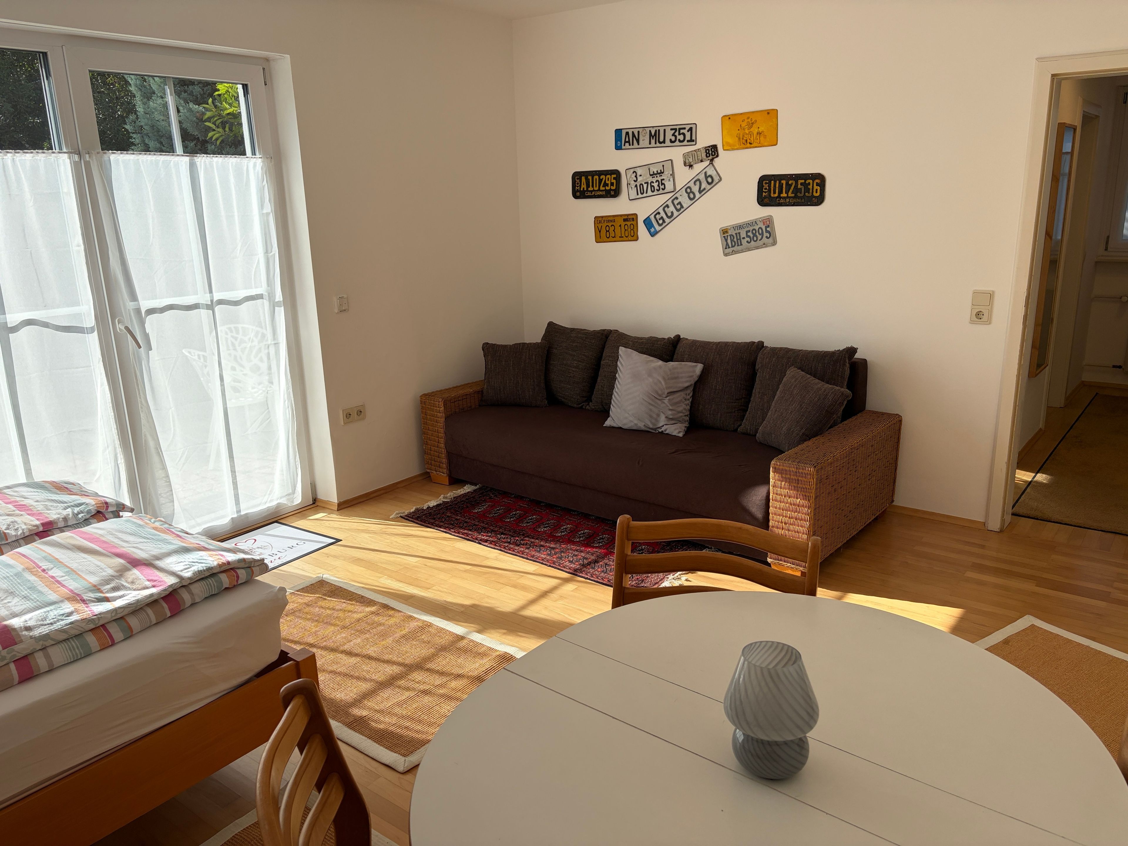 Una sala de estar acogedora con un sofá marrón, una mesa de comedor con un florero y una pared decorada con diferentes matrículas.