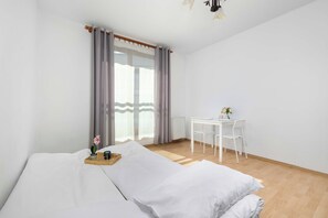 A hotel room with a bed, a small table with a chair, and a window with curtains. - Cracow | Dworska 1B | Functional Apartment | Balcony (Kraków)