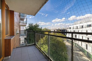 Un balcon donnant sur un paysage urbain, un sol carrelé et une balustrade en verre.