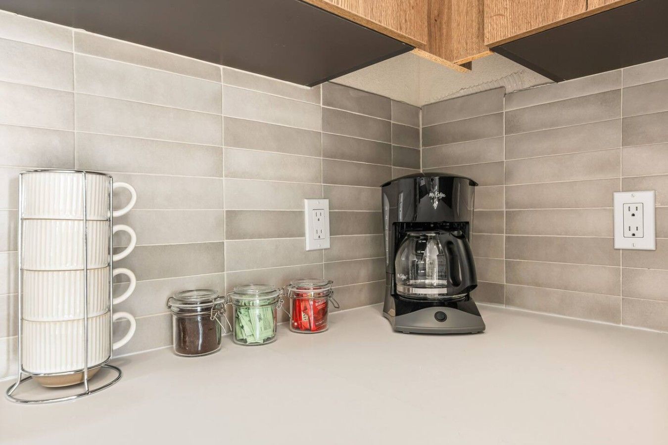 A kitchen with a coffee maker, a mug rack, and three jars of spices.