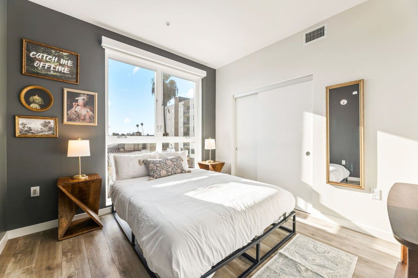Une chambre avec un grand lit, une fenêtre donnant sur un beau paysage, un miroir et des œuvres d’art murales.