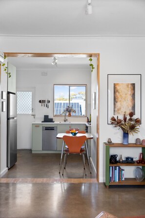 A modern kitchen with a dining area, a view of the outdoors, and a bookshelf with books and decorative items. - The Muse—Convenient City-Fringe Hideaway (Dulwich)