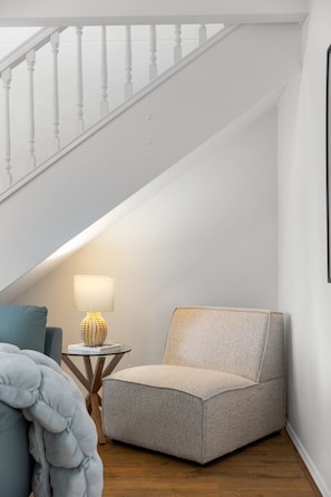 Ein Eckzimmer mit Treppe, einem Sessel, einer Lampe und einem kleinen Tisch.