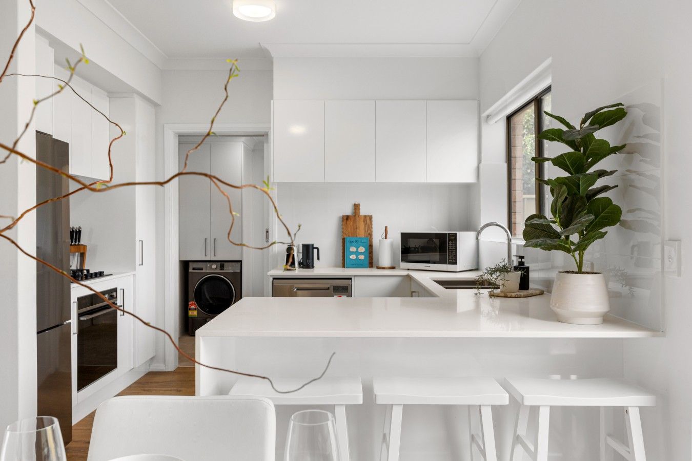 A modern kitchen with white cabinetry, a central island with bar stools, a microwave, a coffee maker, and a potted plant.