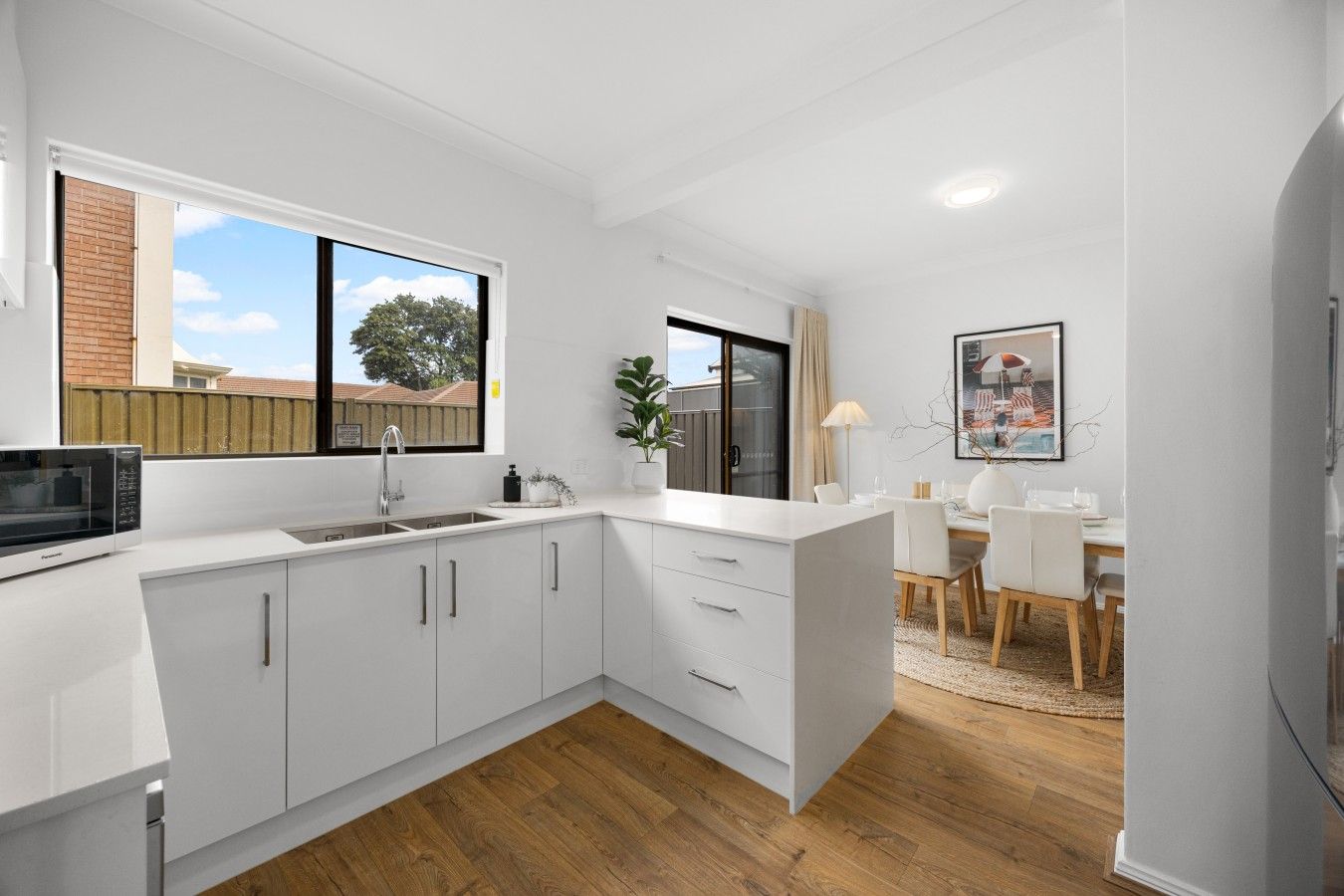 A modern kitchen with white cabinetry, a built-in microwave, and a dining area with a table and chairs.