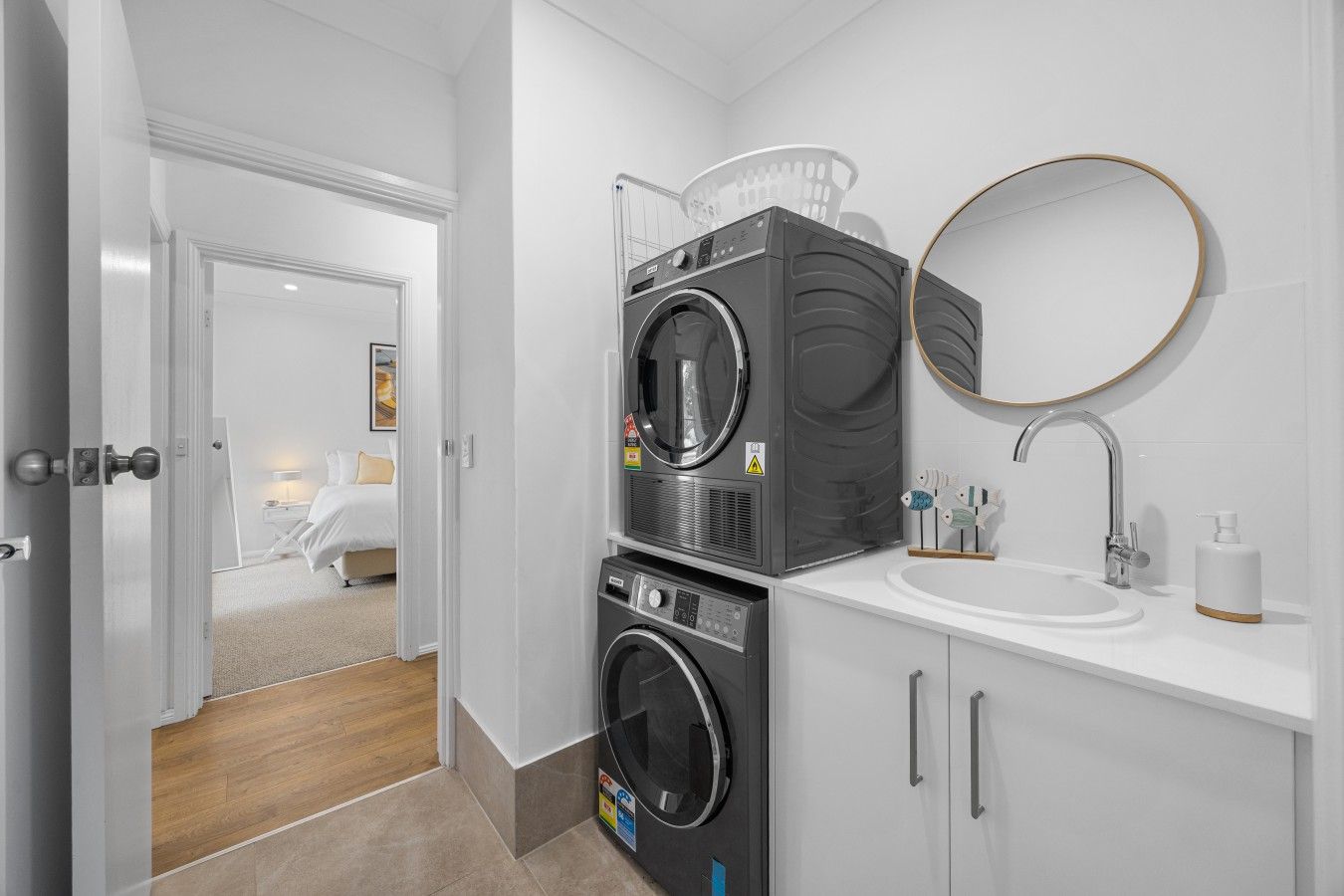 A modern bathroom with a stacked washer and dryer, a round mirror, and a sink with a soap dispenser.