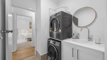 A modern bathroom with a stacked washer and dryer, a round mirror, and a sink with a soap dispenser.