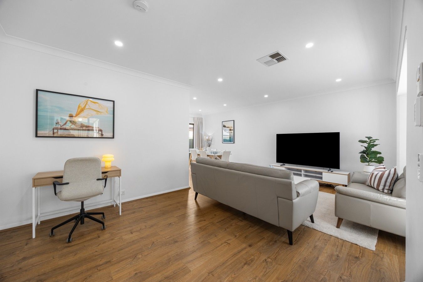 A modern living room with a sofa, a desk with a chair, a flat-screen TV, and a plant.