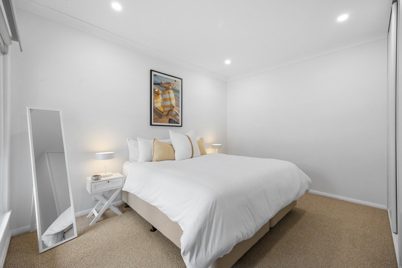 Een hotelkamer met een bed, nachtkastjes, een spiegel en een schilderij aan de muur.