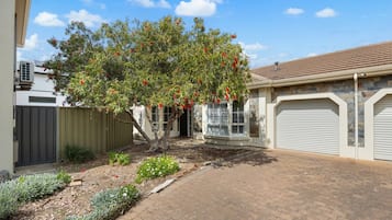 A residential property with a paved driveway, a tree with red flowers, and a garage.