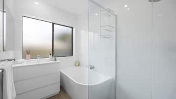 A modern bathroom with a freestanding bathtub, a glass-enclosed shower, and a large window providing natural light.