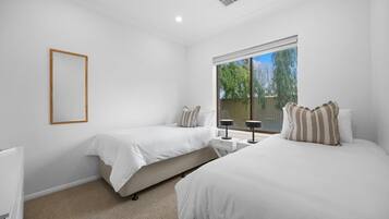 A bedroom with two beds, a window with a view of greenery, and a white ceiling with a vent.