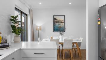 A modern kitchen with white cabinetry, a dining area with a table set for four, and a large window with a view of the outdoors.
