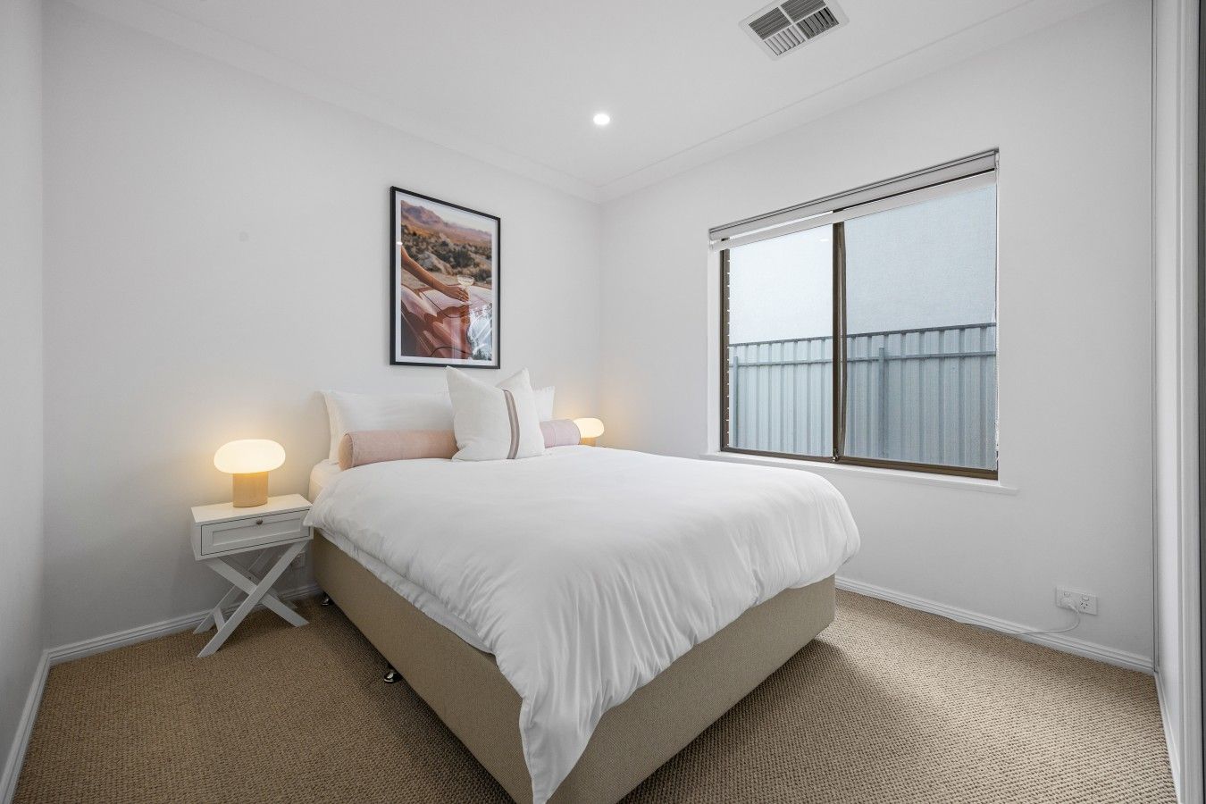 A bedroom with a bed, bedside lamps, a framed picture, and a window.