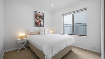 A bedroom with a bed, bedside lamps, a framed picture, and a window.