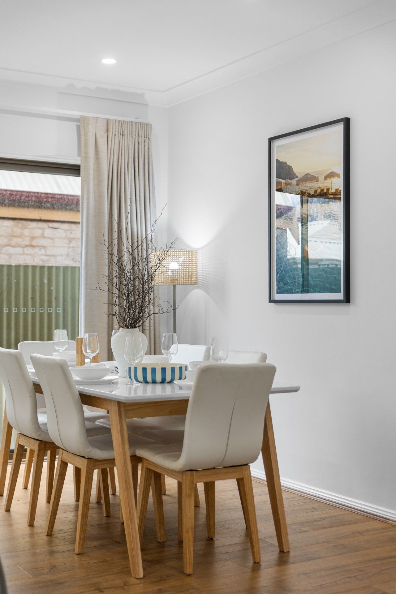 A dining area with a round table, white chairs, and a framed picture on the wall.