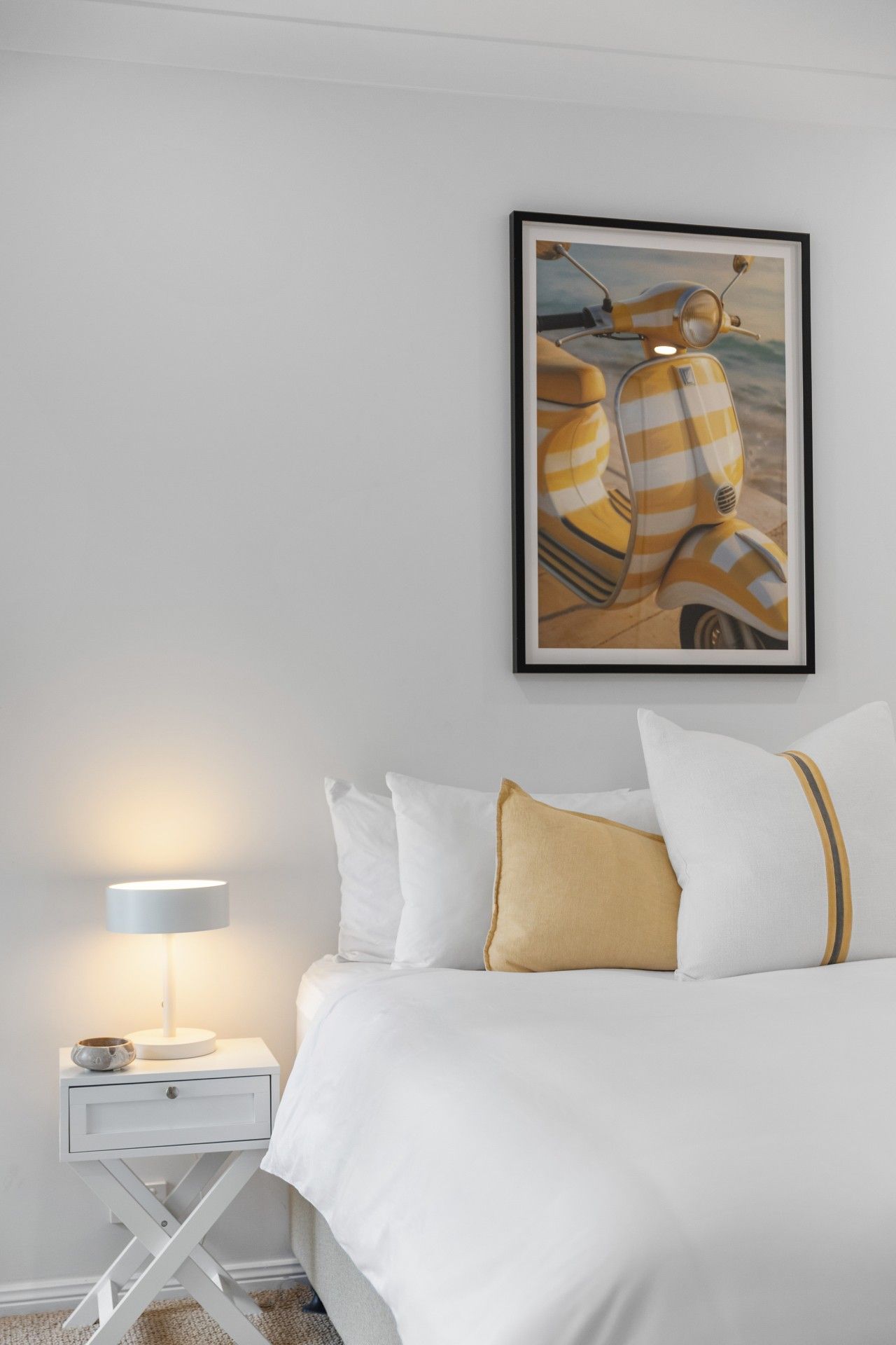 A bedroom with a bed, pillows, a nightstand, a lamp, and a framed picture on the wall.