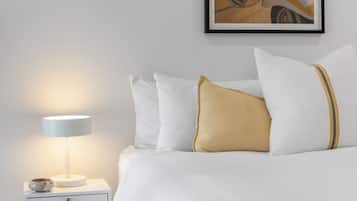 A bedroom with a bed, pillows, a nightstand, a lamp, and a framed picture on the wall.